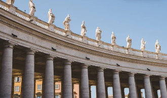 Vista en perspectiva de la columnata de Bernini en la Plaza de San Pedro con estatuas de santos sobre la balaustrada bajo un cielo despejado Vista en perspectiva de la columnata de Bernini en la Plaza de San Pedro con estatuas de santos sobre la balaustrada bajo un cielo despejado