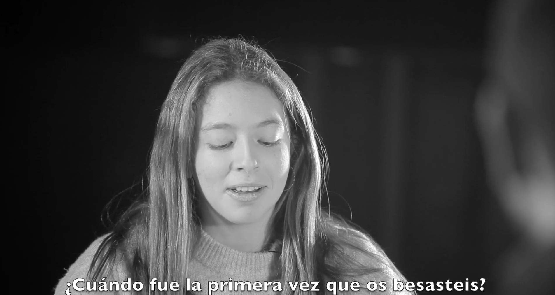 Retrato en blanco y negro de una joven hablando con el subtítulo ¿Cuándo fue la primera vez que os besasteis? en la parte inferior